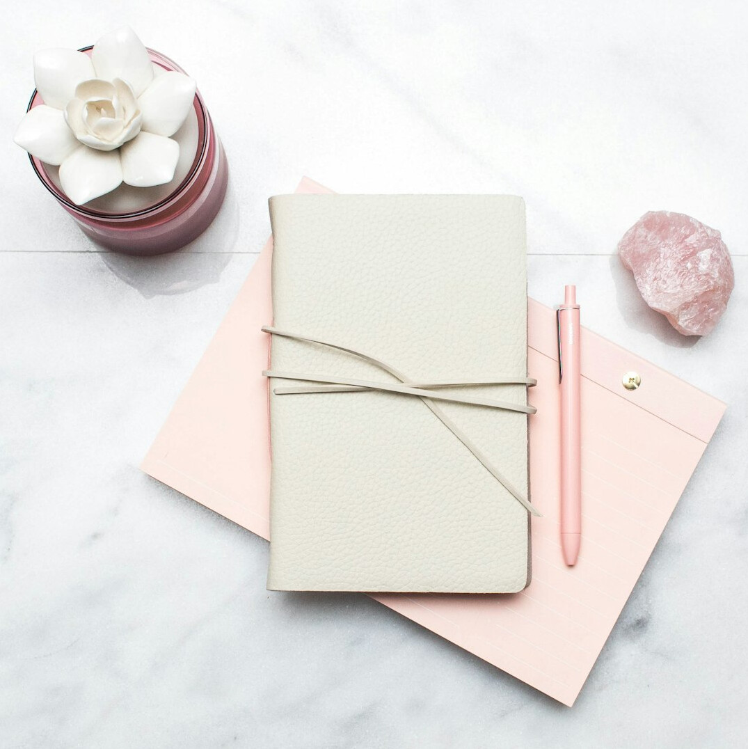 Notebook and pen on a wooden desk with a magnifying glass
